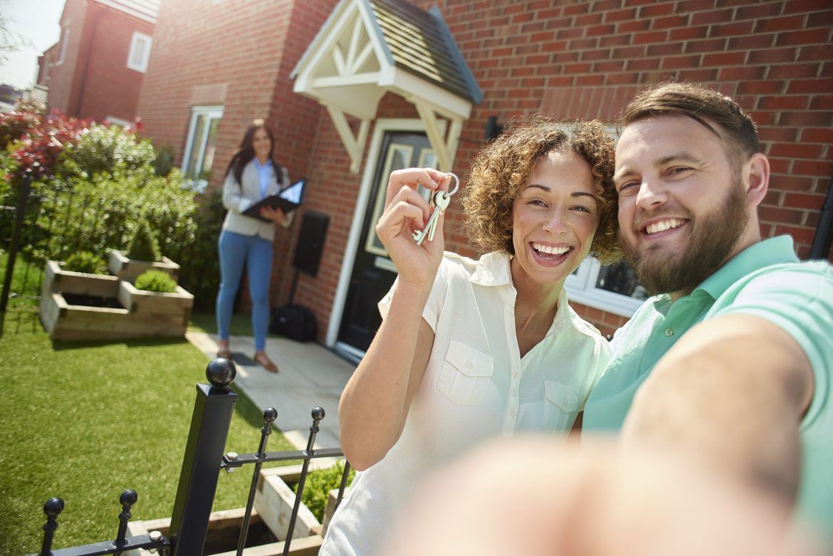 a young couple celebrate getting the keys to their new home by taking a selfie in the garden.