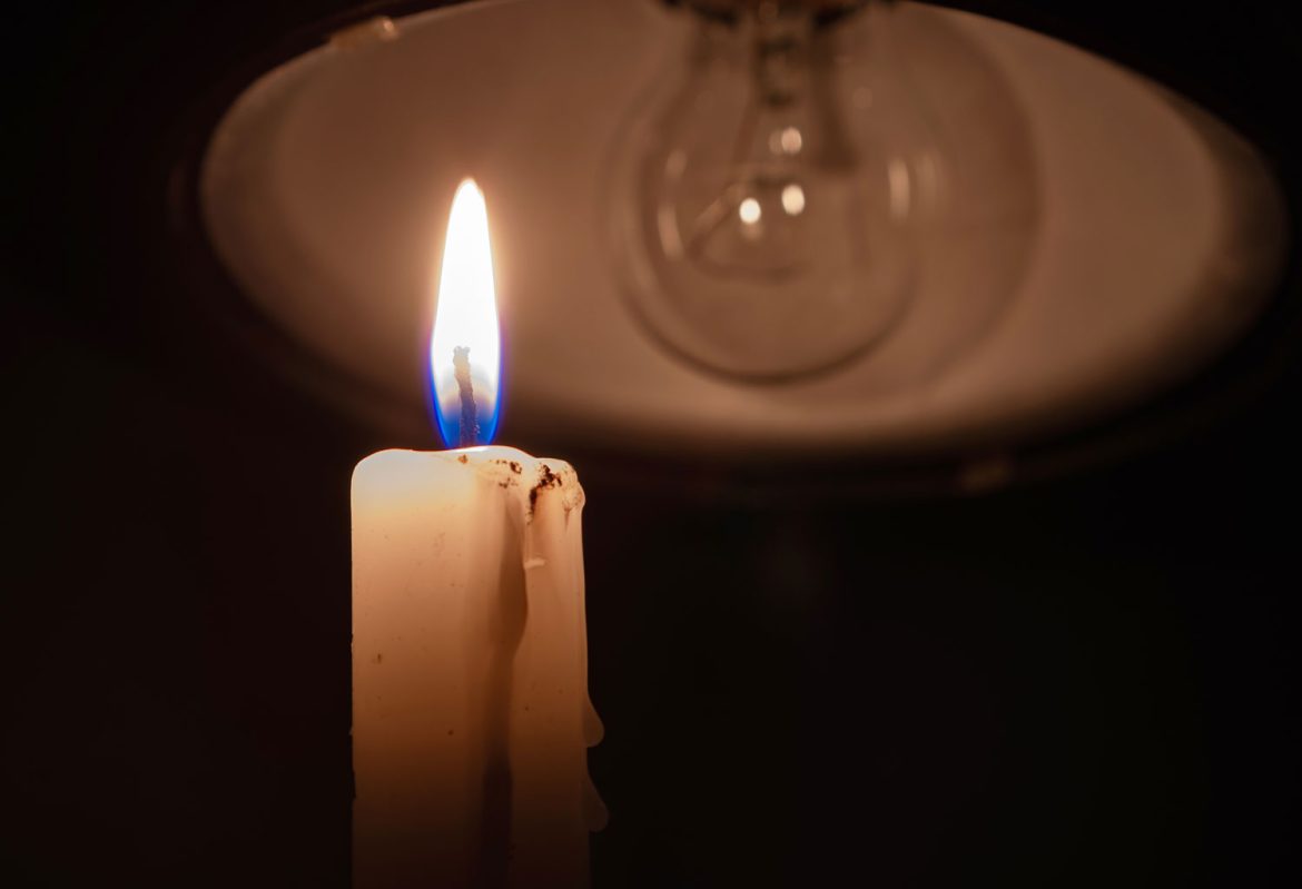 Lit candle in front of an unlit light bulb