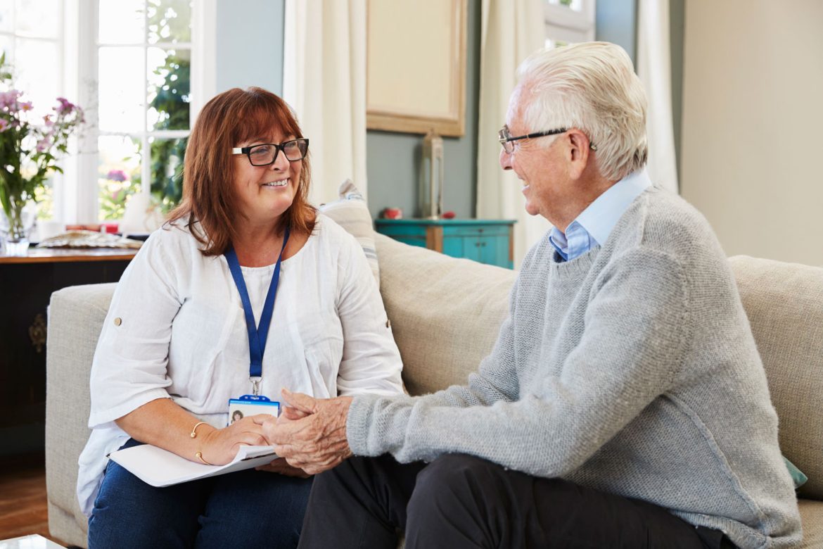 A female social worker talks to an old man while sat on a sofa