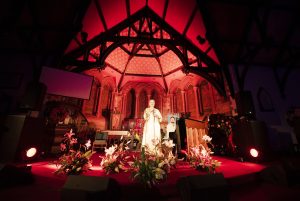 Lapsley performs on the pulpit at St Nicholas Church, Halewood. the stage is illuminated in a red glow and lillies adorn the front of the stage.