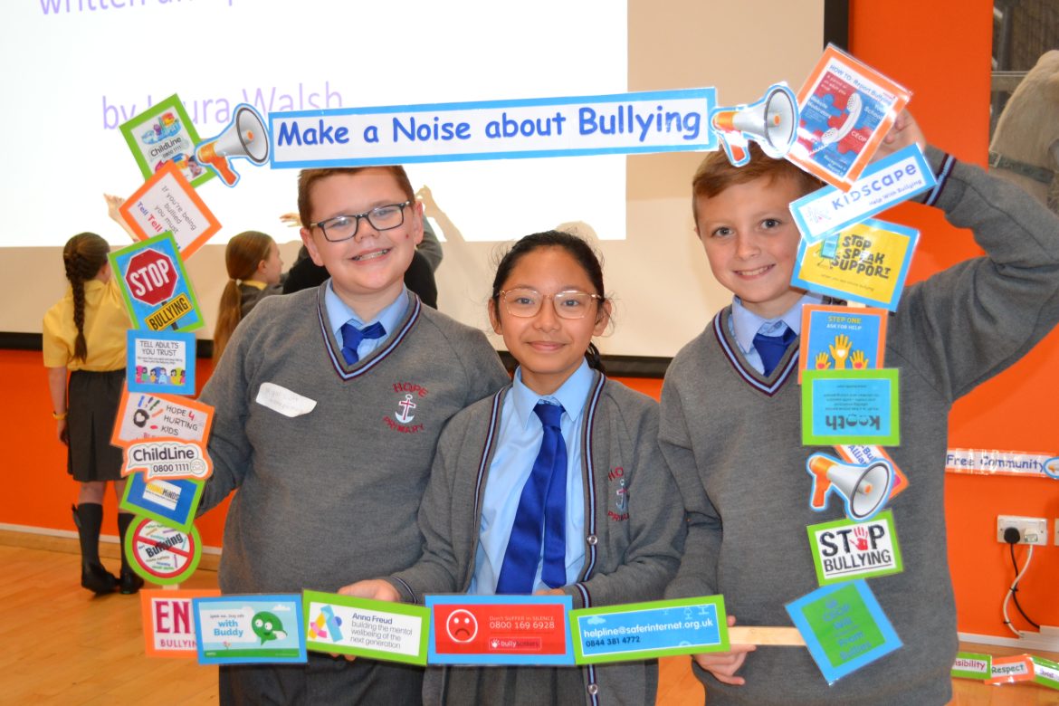 3 school children stand with a frame. The frame says Make a Noise About Bullying