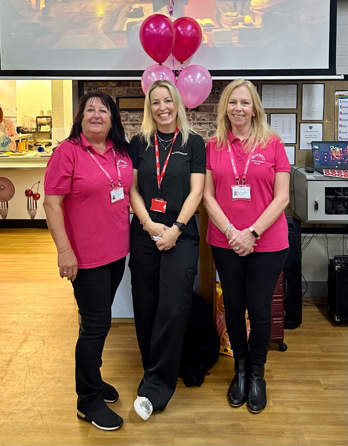 Three women pose in front of a heart balloon at a charity event.