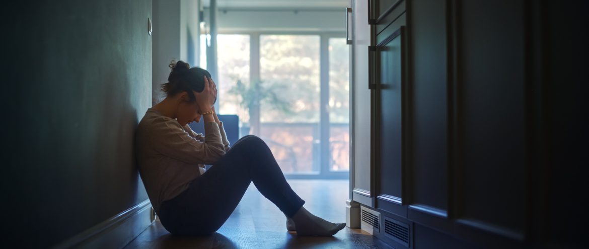 Sad Woman Sitting on the Floor In the Hallway of Her Apartment, Covering Face with Hands.