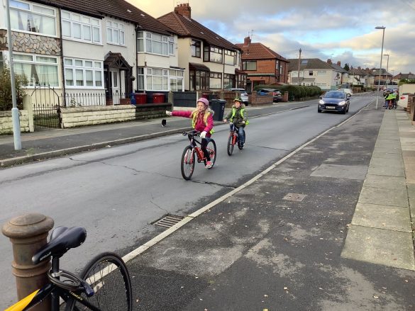 Malvern Bikeability1 Children in high vis vests and helmets cycling along a road whilst signalling to turn right