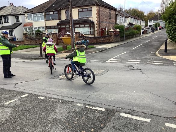 Malvern Bikeability2 Man in high vis vest and helmet supervises children as they cycle along a road.