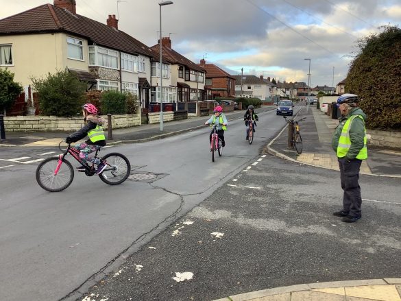 Malvern Bikeability3 Man in high vis vest and helmet supervises children as they cycle along a road.