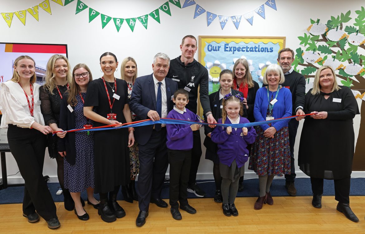 A group of people holding a blue and red ribbon that is to be cut to mark the official opening of the new education centre. Primary ages children stand at the front.