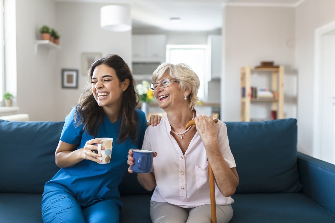 Photo of Happy Young Female Caregiver and Elderly Female Drinking Coffee While Sitting in the Living Room.